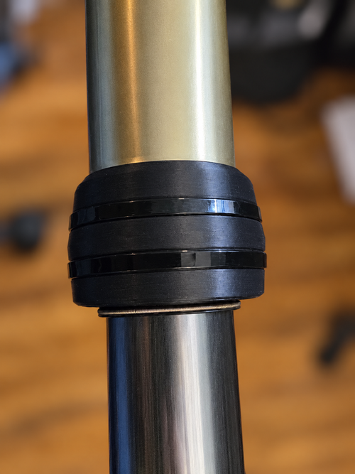 Plain-black M4 Enduro 43mm KYB fork guard installed around the outer fork housing, secured with two black zip ties. No white logo. Background blurred.