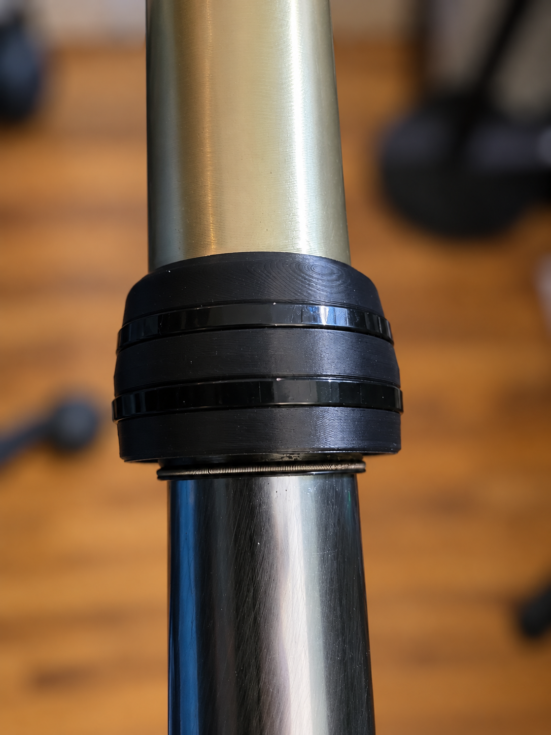 Plain-black M4 Enduro 43mm KYB fork guard mounted around the gold outer fork housing with two black zip ties, with the polished lower tube visible. No white product logo. Background blurred.